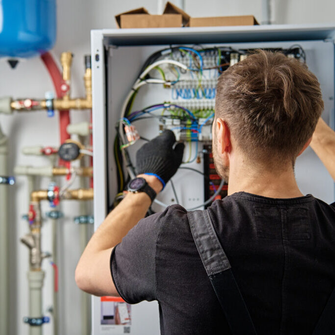 Technician working on internal wiring of heat pump, inspecting electrical connections. Specialist servicing heating and cooling system. Electrician with screwdriver tightening screws on control panel